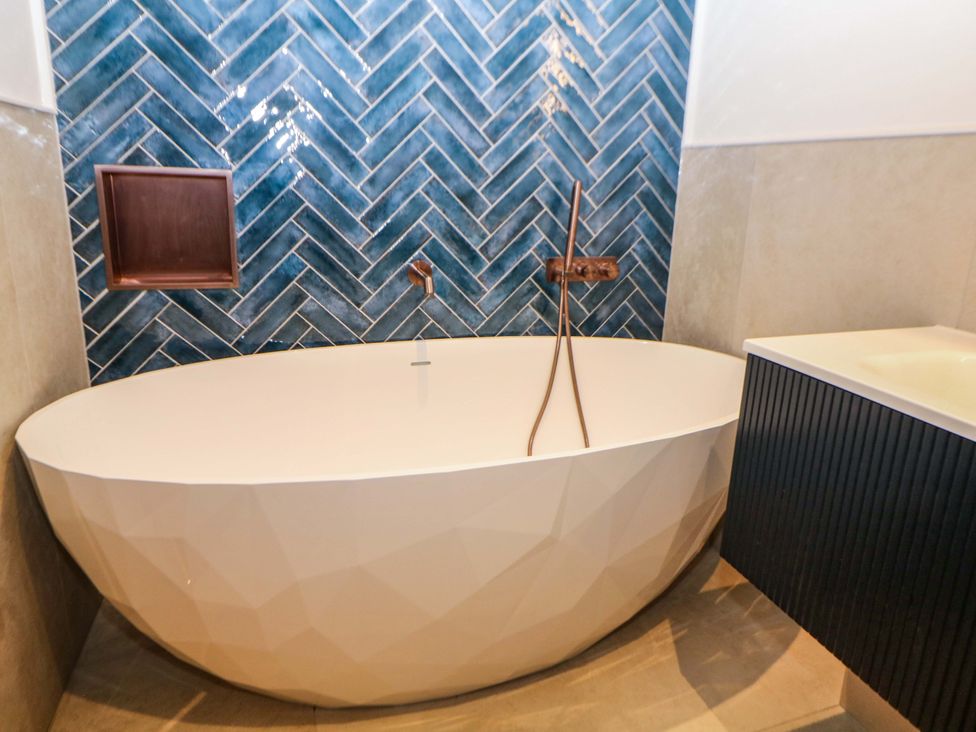 A bathroom with a bathtub and wall tiles at The Reading Room in Hope Valley