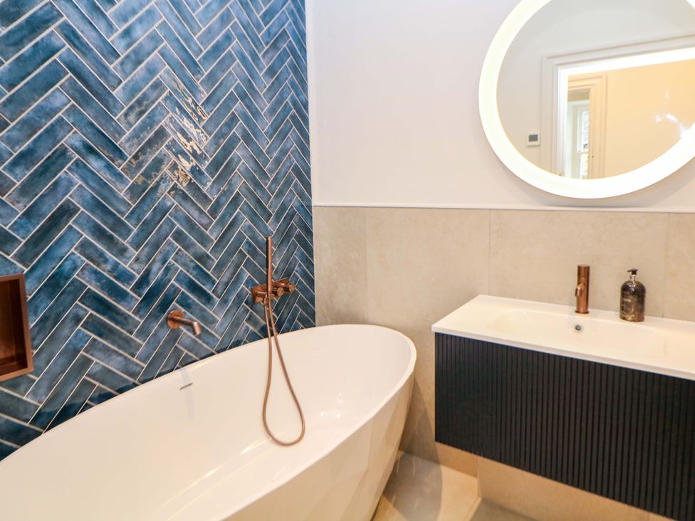 A bathroom with a bathtub, sink, and mirror at The Reading Room in Hope Valley