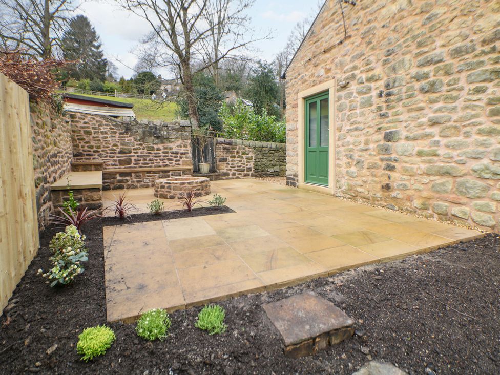 A garden with a stone wall, patio, and plants at The Reading Room in Hope Valley