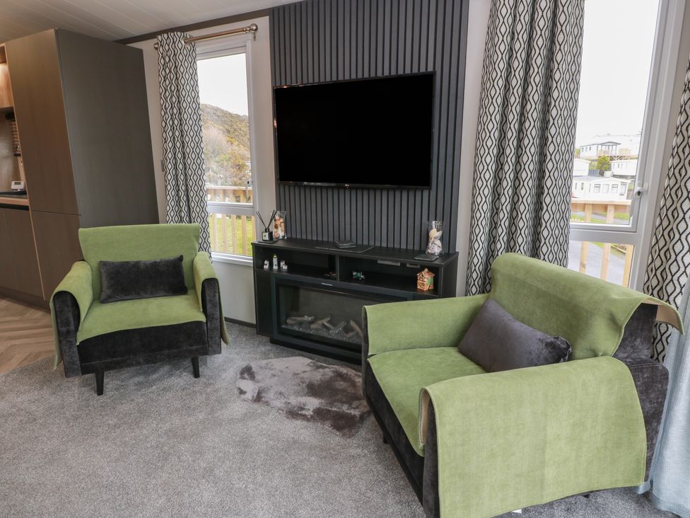 A living room with green armchairs and a television at Willow's Way in Stranraer
