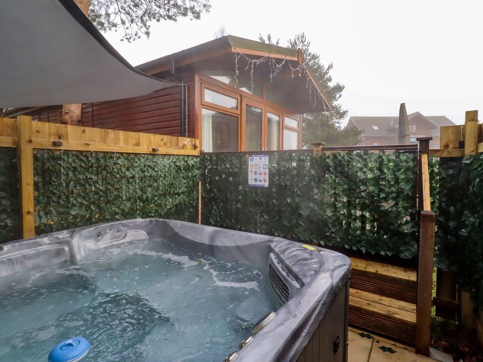 An outdoor area with a hot tub and wooden cabin at Harper's Hideaway near Felmoor Holiday Park in Felton