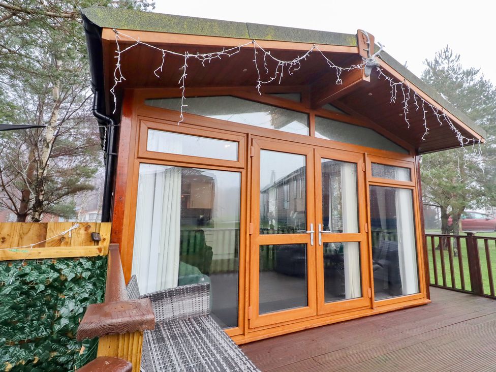 A wooden cabin with large windows and a deck at Harper's Hideaway Felmoor Holiday Park near Felton