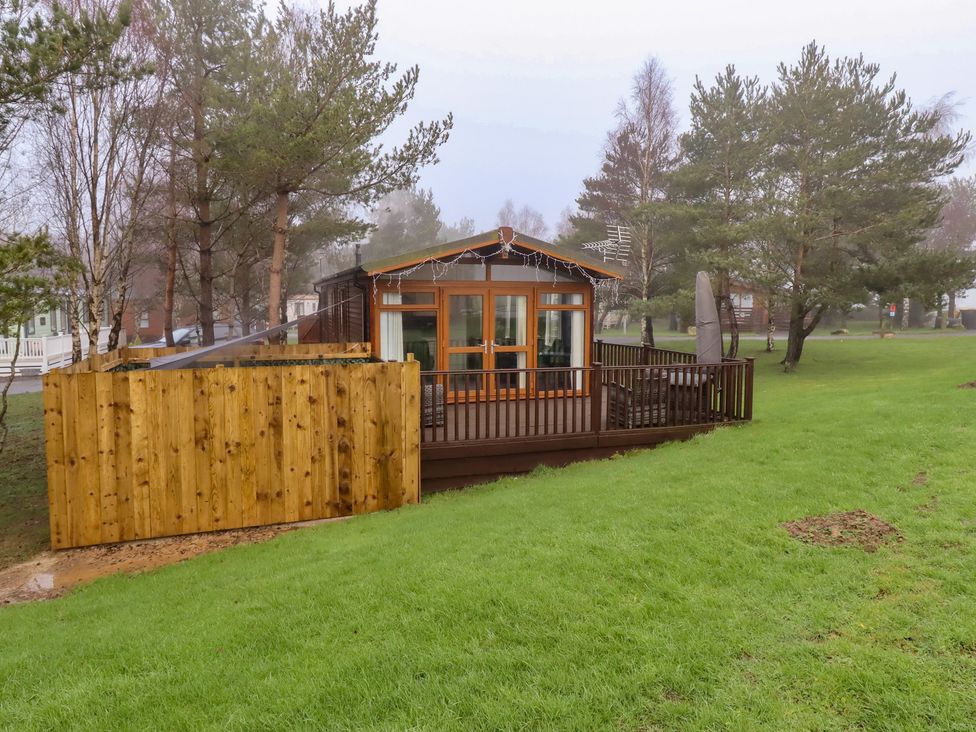 A cabin with a deck and wooden fence at Harper's Hideaway near Felmoor Holiday Park near Felton