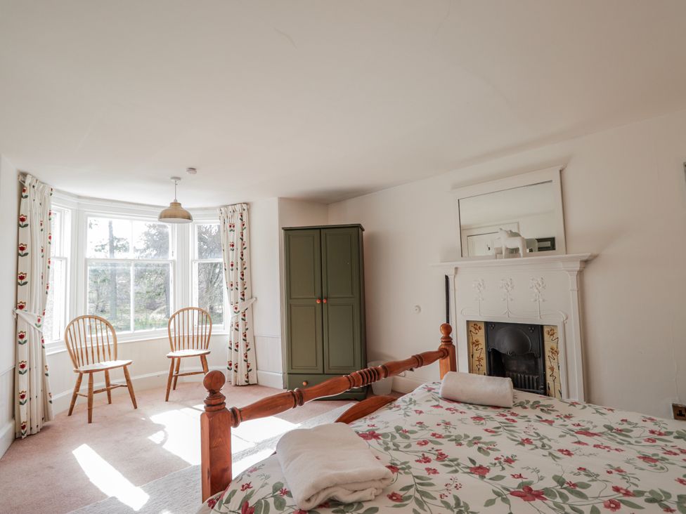 A bedroom with a bed and chairs next to a window at Achnagonlin House in Grantown-on-Spey