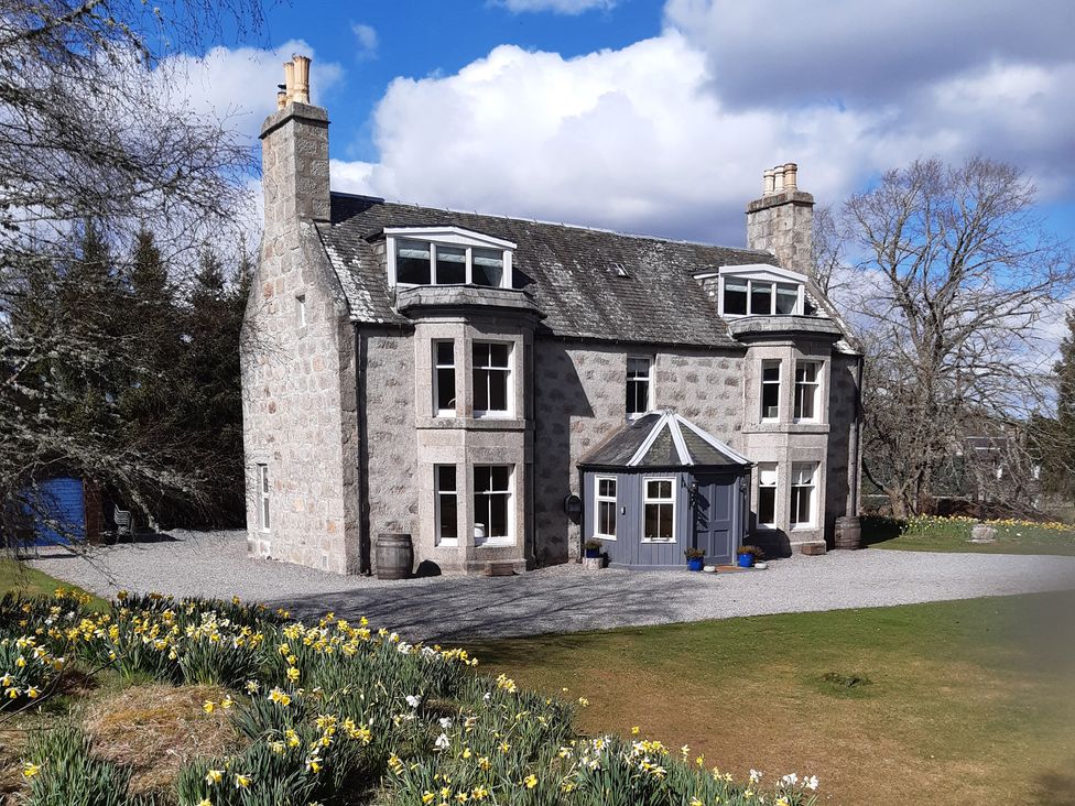 A house with a gravel driveway and flower bed at Achnagonlin House in Grantown-On-Spey