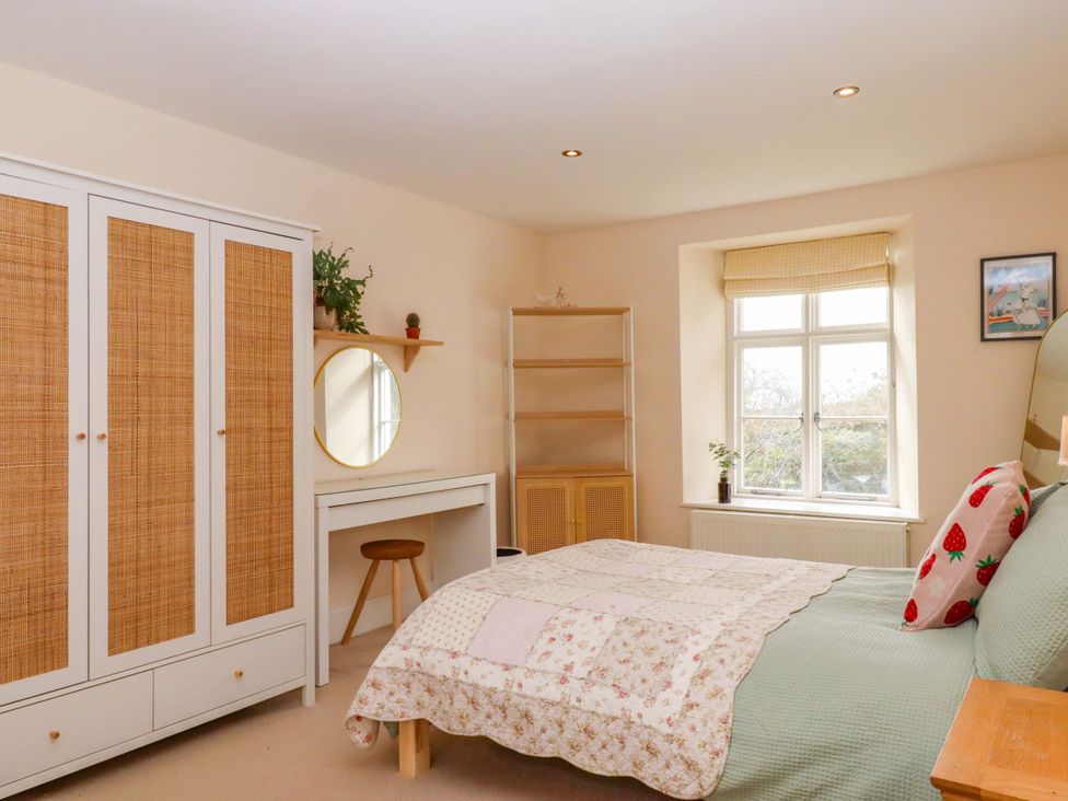 A bedroom with a wardrobe, mirror, and table at The Mill House in Newton Abbot