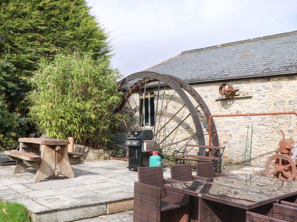 A garden with an outdoor table, chairs, barbecue grill, and water wheel at The Mill House in Newton Abbot