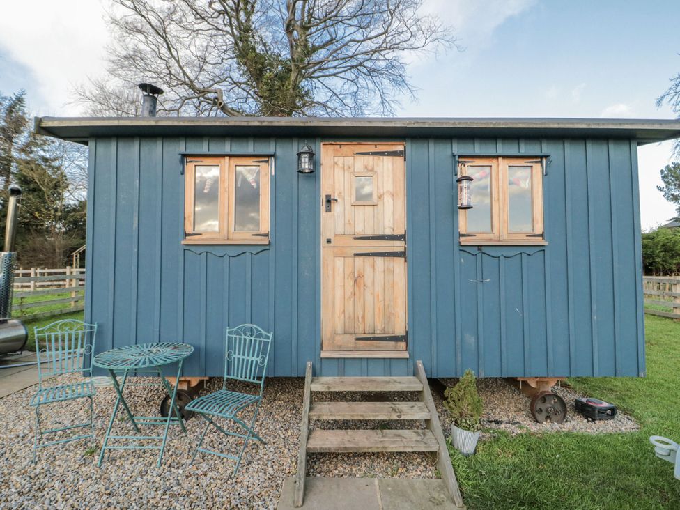 A blue hut with wooden door and outdoor seating at Honeysuckle Hut, Potto Grange Farm, Northallerton
