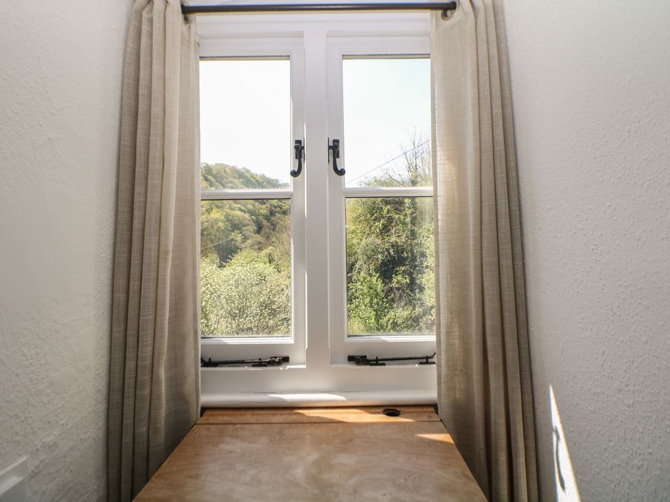 A window with curtains and wooden table at Honeysuckle Cottage