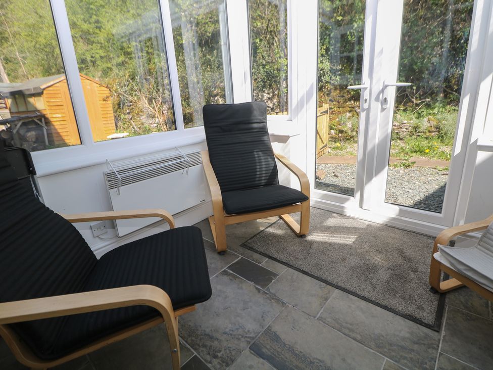 A conservatory with chairs and a door leading outside at Honeysuckle Cottage