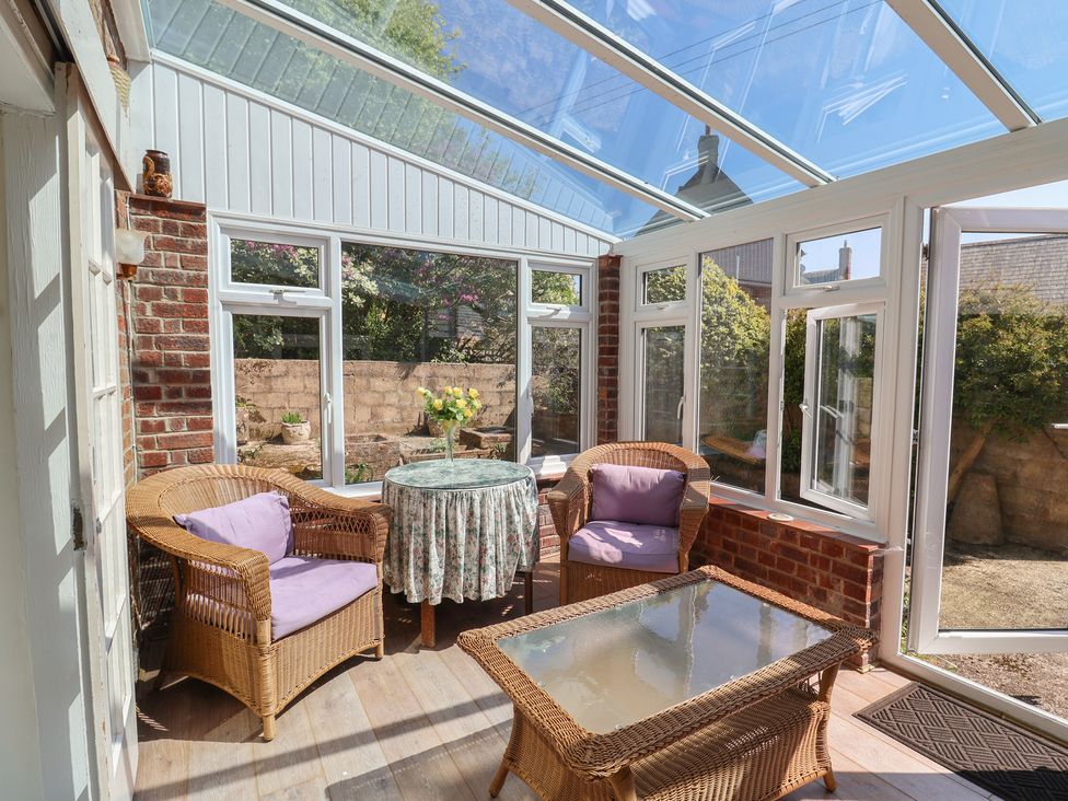 A conservatory with wicker furniture and a glass table at Goulds Farmhouse in Milborne St Andrew