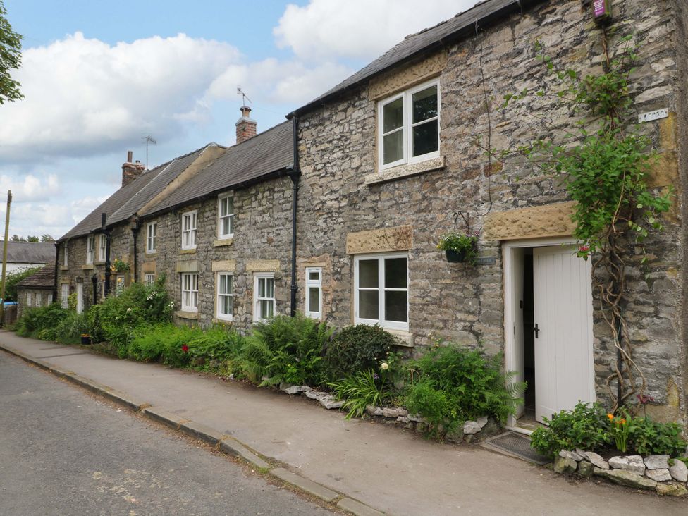 A stone building with windows and plants at Hope Cottage in Great Longstone
