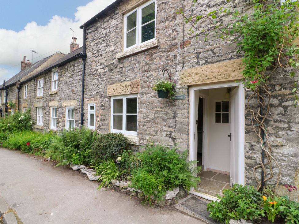 An outdoor view of a stone cottage entrance with garden plants at Hope Cottage in Great Longstone