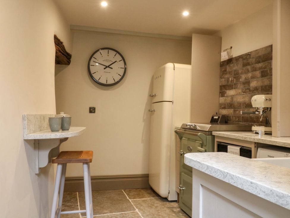 A kitchen with a refrigerator, sink, and clock at Hope Cottage in Great Longstone