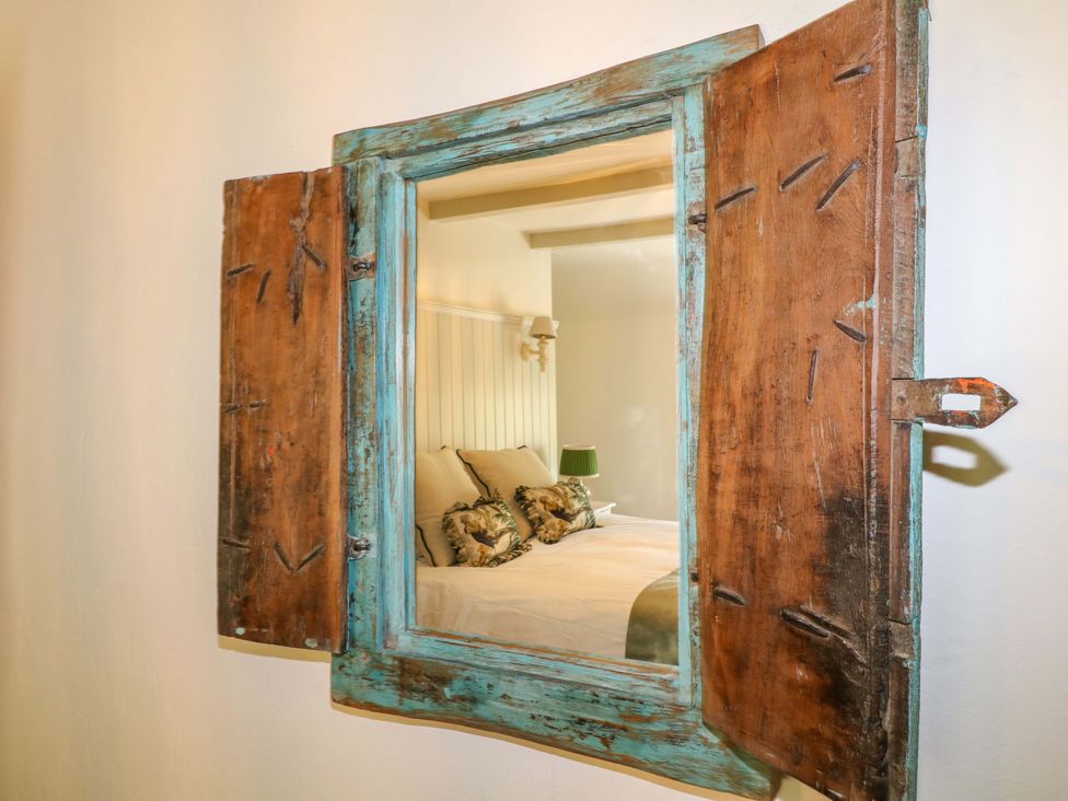 A mirror with wooden frame reflecting a bed with cushions at Hope Cottage in Great Longstone
