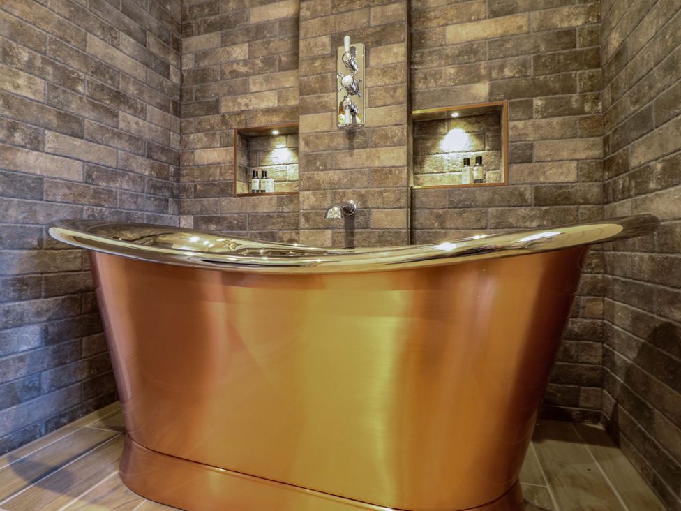 A bathtub in a bathroom with stone walls and shelves in Hope Cottage Great Longstone