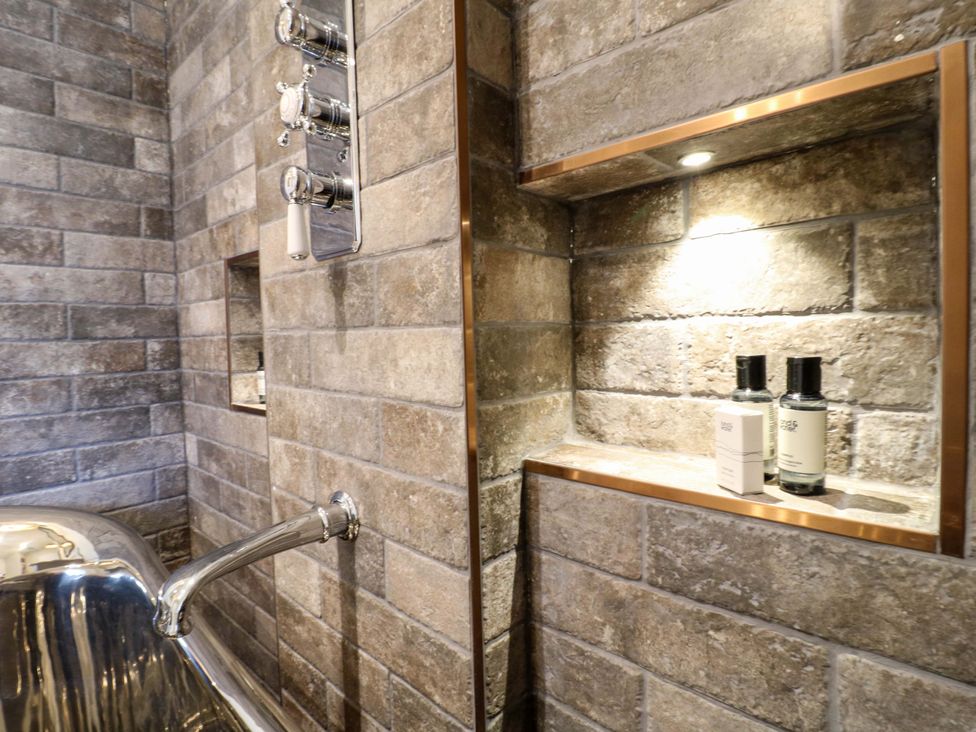 A bathroom with a bathtub and shelves for toiletries at Hope Cottage in Great Longstone