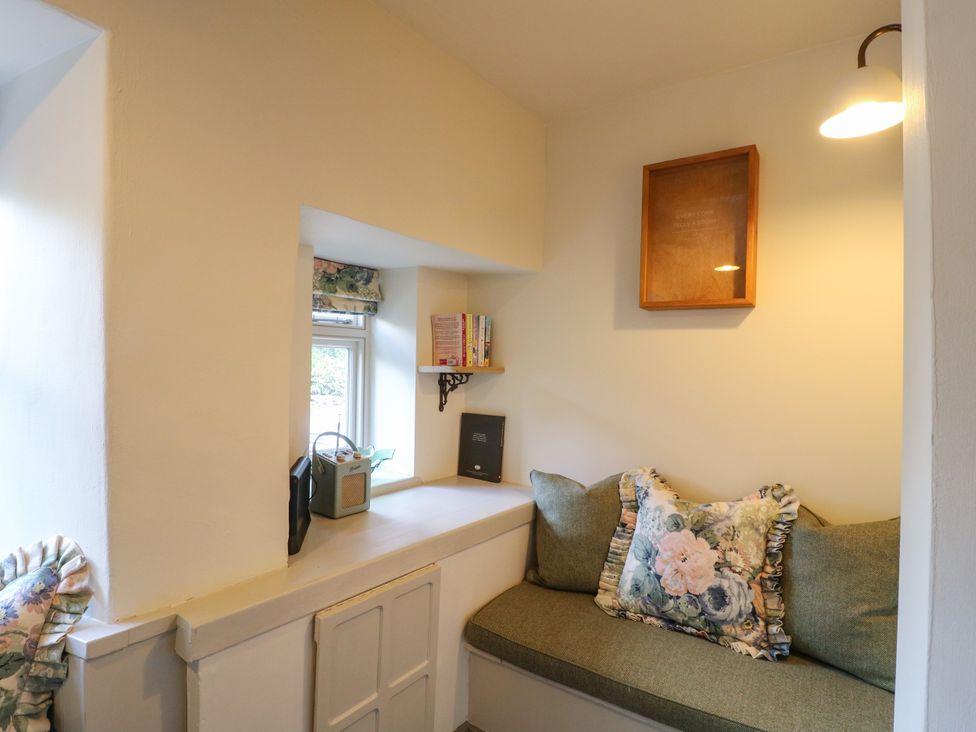 A snug with a window, bookshelf, and cushion at Hope Cottage in Great Longstone