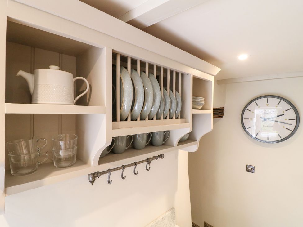 A kitchen with shelving displaying tableware and a clock at Hope Cottage in Great Longstone
