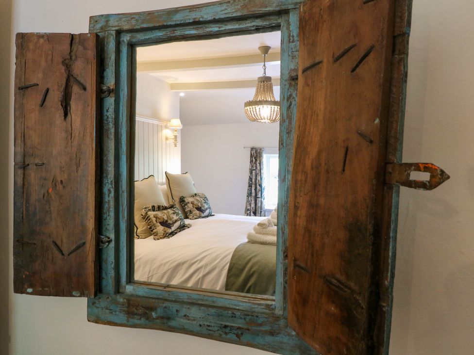 A mirror reflecting a bedroom with a bed and curtains at Hope Cottage in Great Longstone