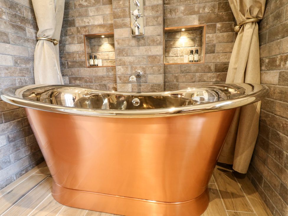 A bathroom with a copper bathtub and stone wall at Hope Cottage in Great Longstone