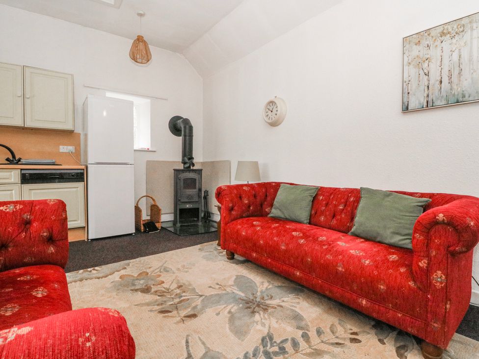 A living room with a red sofa and a kitchen area at Oak Killean Farmhouse Cottages near Inveraray