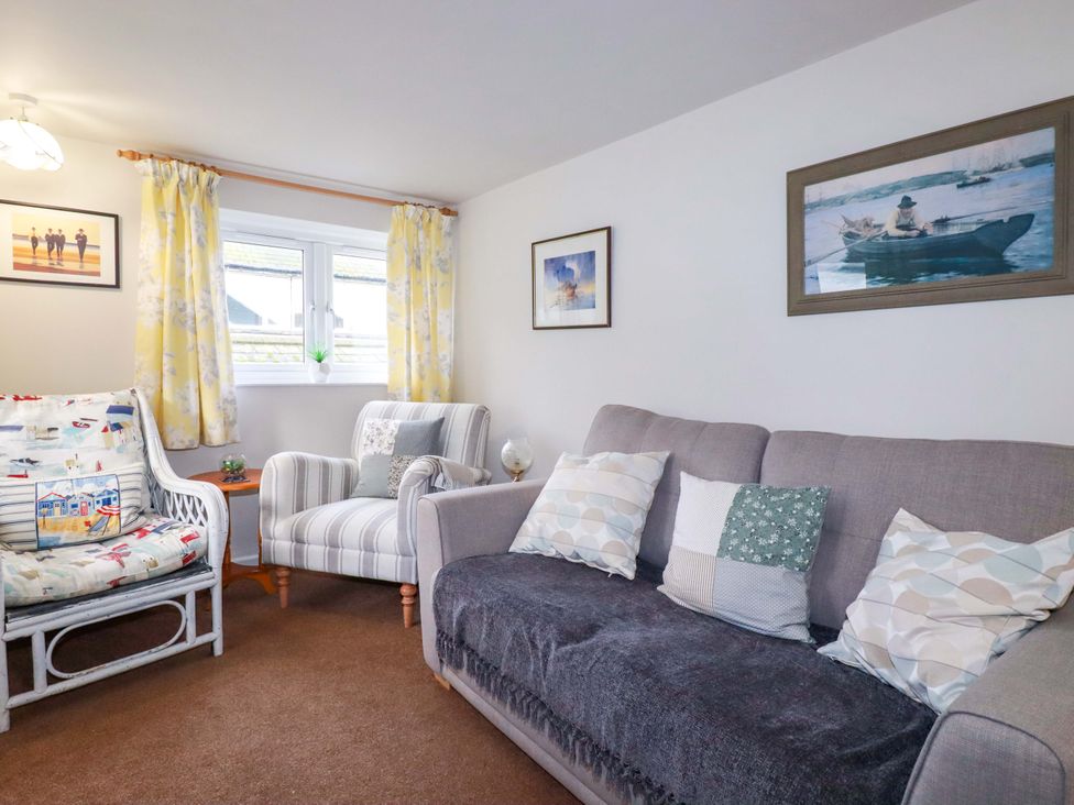 A living room with a sofa, two chairs, and wall art at The Penthouse in Looe