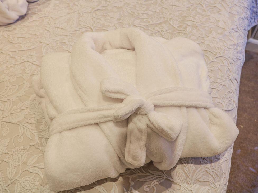 A folded white bathrobe on a bed at Courtyard View in Ashbourne