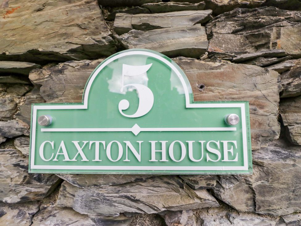 A house sign reading 5 Caxton House on a stone wall in Windermere