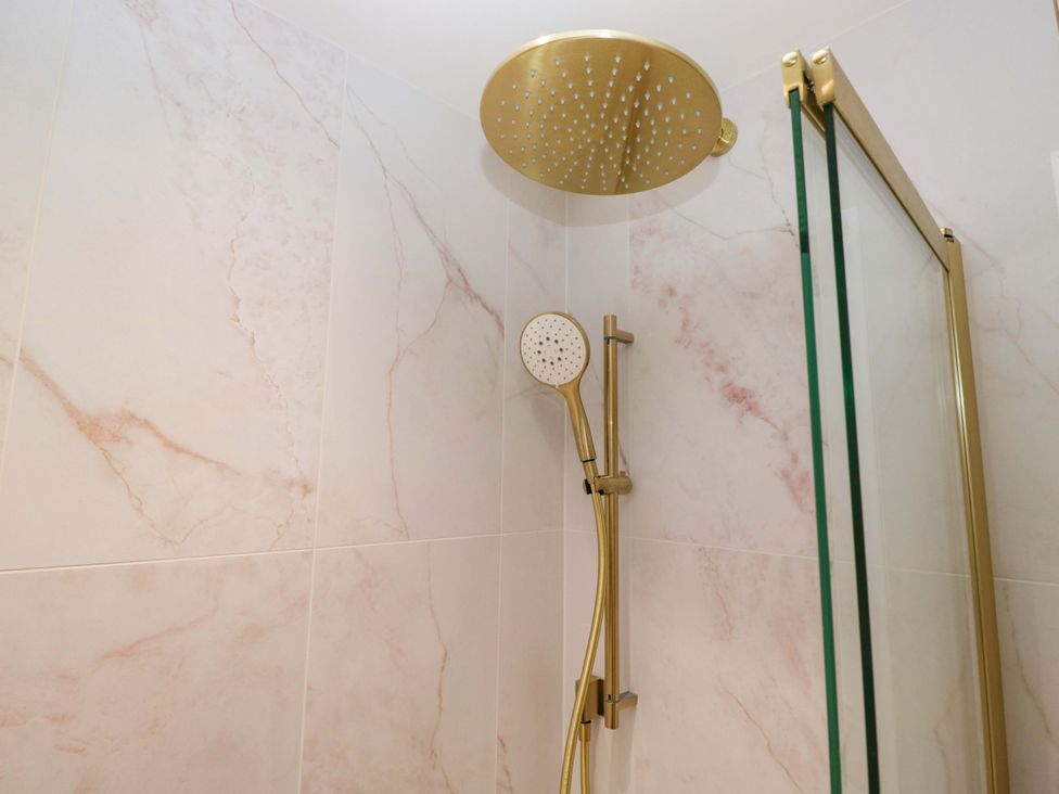 A shower with gold fixtures and marble tiles at Flat 5 Caxton House in Windermere