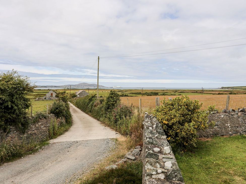 A road leading to a field with houses and the ocean at Bodlasan Groes Cottage in Holyhead