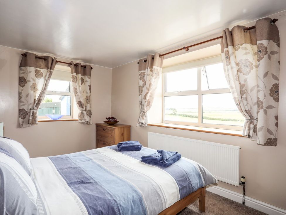 A bedroom with a bed and windows showcasing a view at Bodlasan Groes Cottage in Holyhead