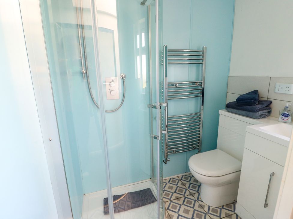 A bathroom with a shower, toilet, towel rack, and sink at Bodlasan Groes House in Llanfachraeth