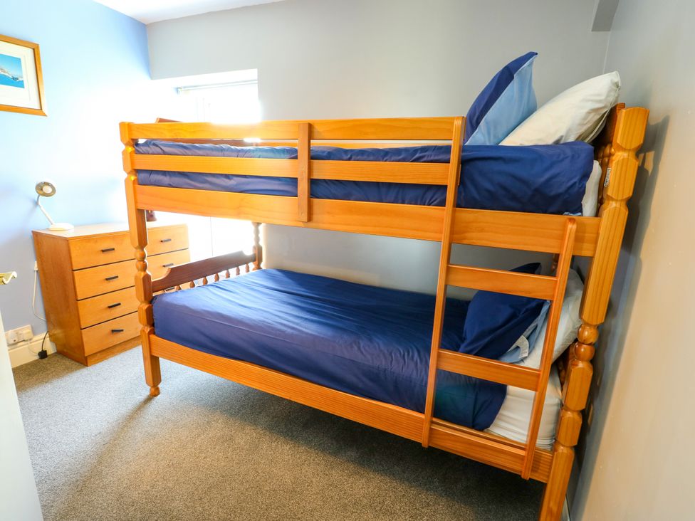 A bunk bed with blue sheets and dresser at Bodlasan Groes House Llanfachraeth