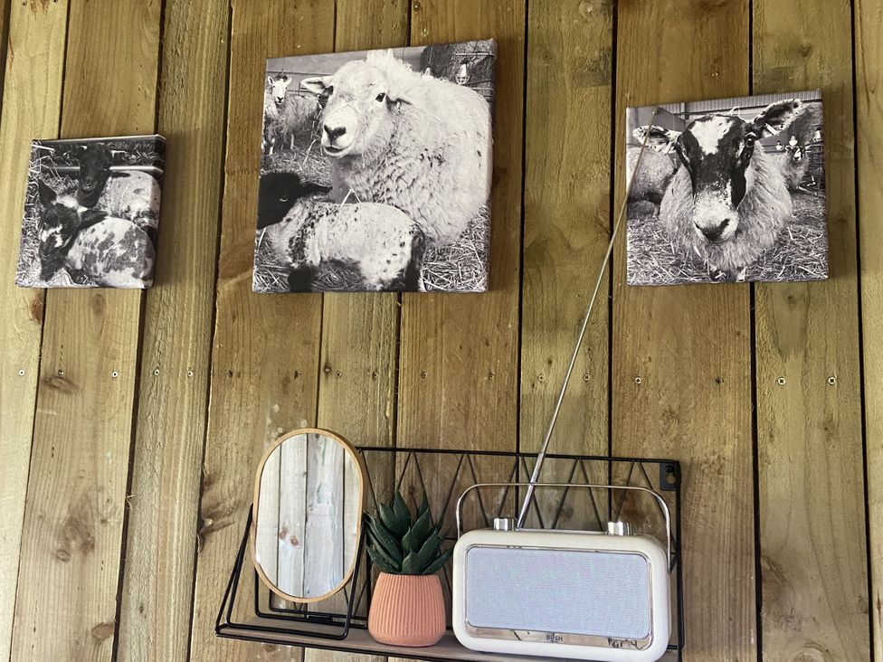 A wall with sheep photos, a mirror, plant, and a radio at The Suffolk Hut in Lower Peover, Cheshire