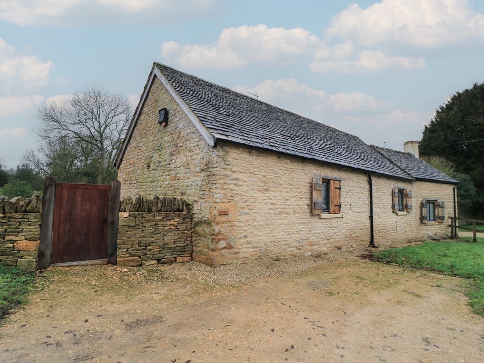 A cottage with a stone wall and wooden gate at The Forge in Broadwell near Stow-On-The-Wold