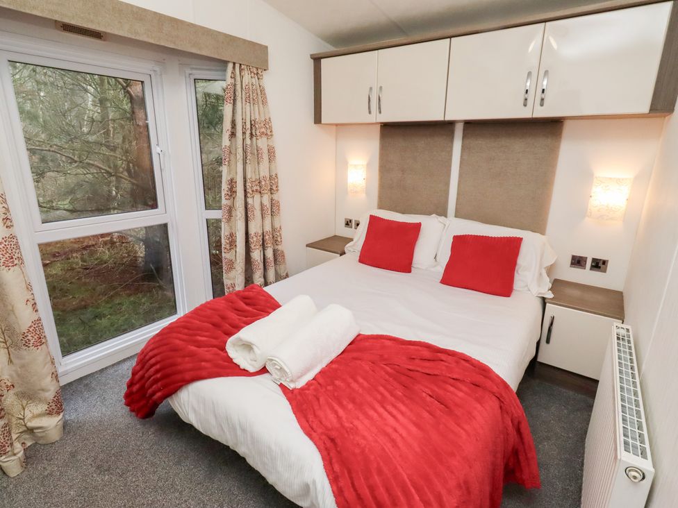 A bedroom with a bed and windows at Chloe's Cabin near Felmoor Holiday Park near Felton