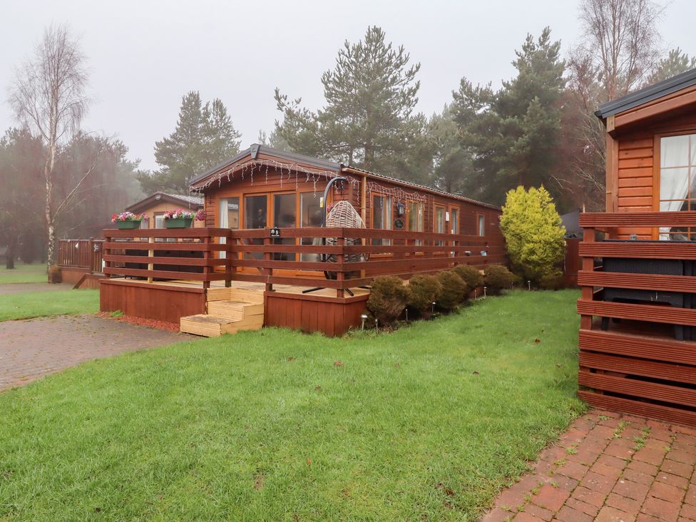 A wooden cabin with a deck and fence at Chloe's Cabin in Felmoor Holiday Park near Felton