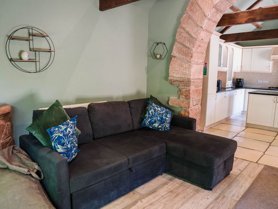 A living room with a sofa and kitchen area at Carwinley Mill House Cottage near Longtown