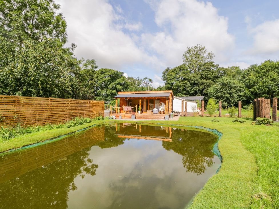 An outdoor area with a pond and a wooden cabin at The Chard in Carlisle