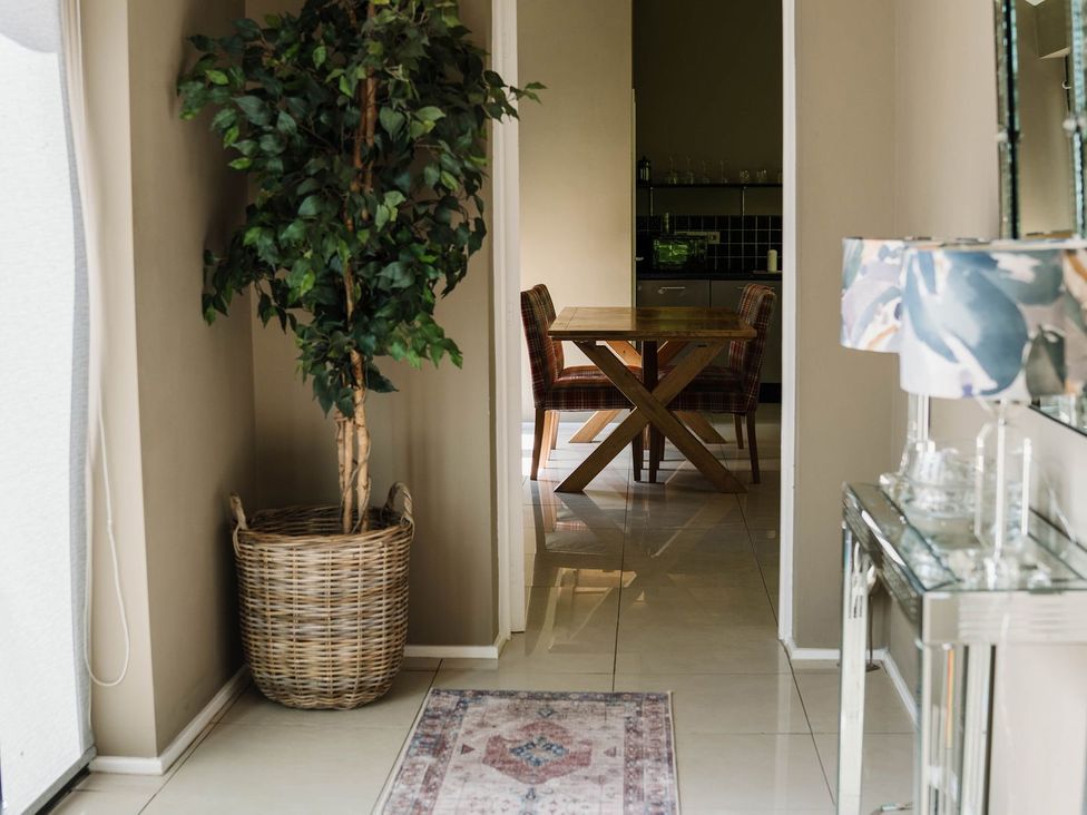 A hallway with a plant and table leading to a kitchen at The Heronry in Carlisle