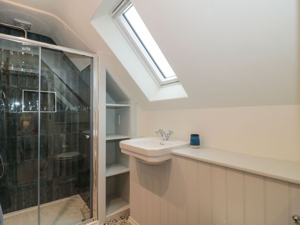 A bathroom with a shower, sink, and shelf at Manor Cottage in Carterton, Oxfordshire