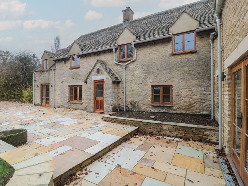 A stone house with a patio and flower bed at Manor Cottage in Carterton, Oxfordshire