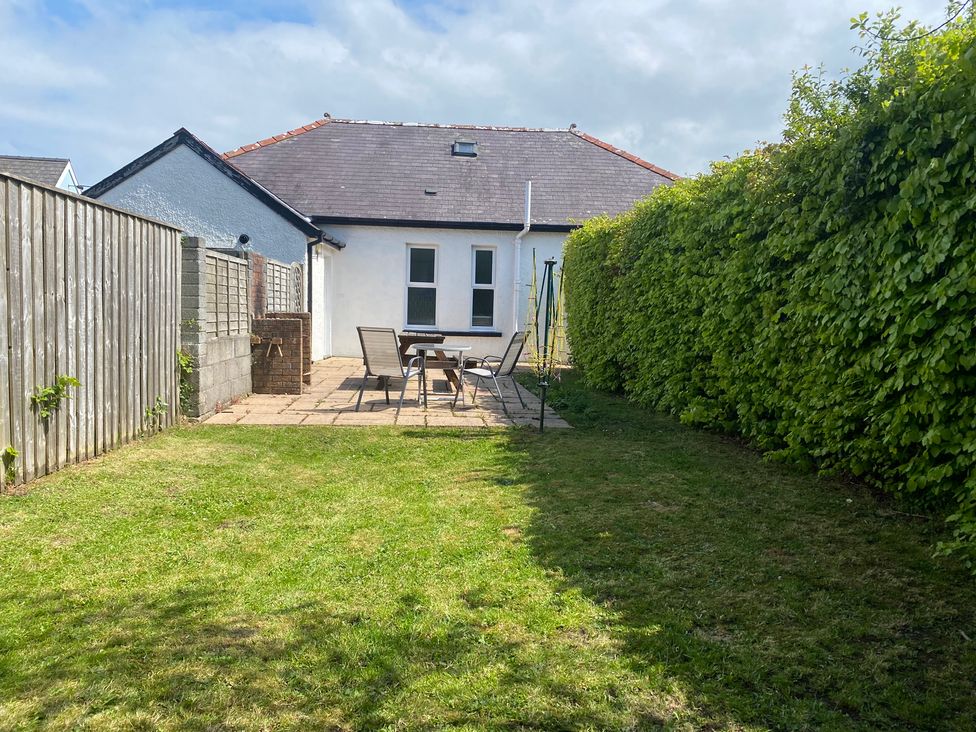 A garden with a house, patio table, chairs, and a swing set at Kenvor Newport, Pembrokeshire