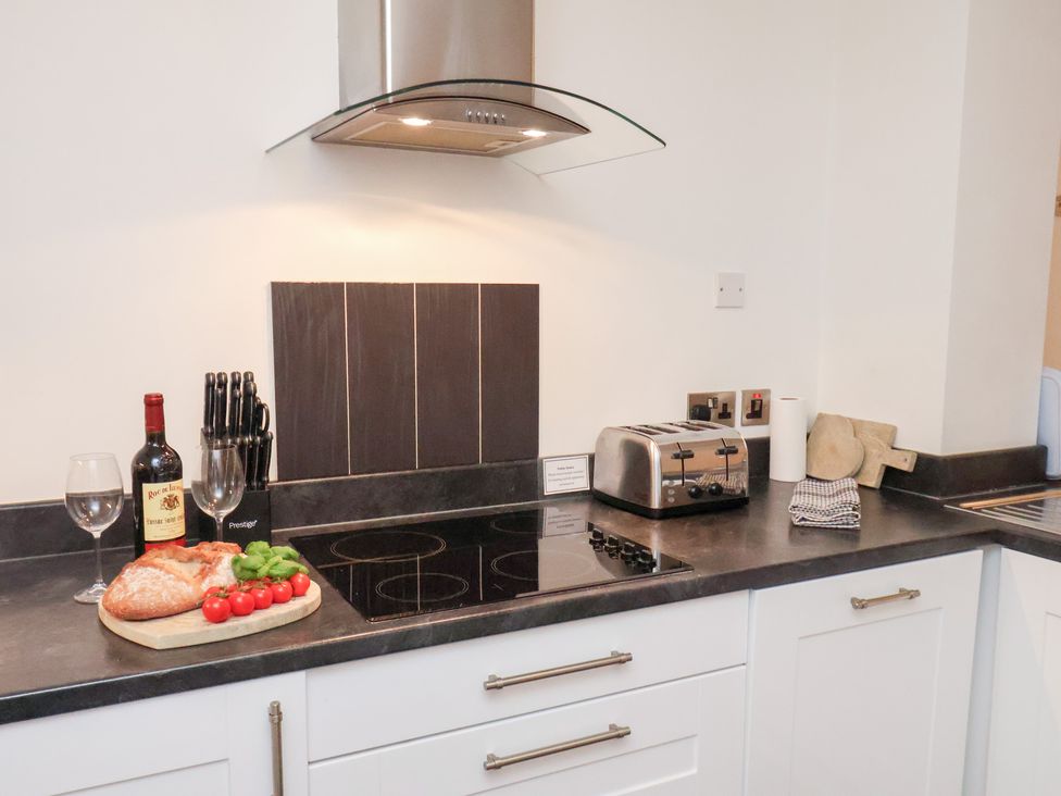 A kitchen with a wine bottle, glasses, and vegetables on the counter at One Union Mill - garden apartment in Whitby