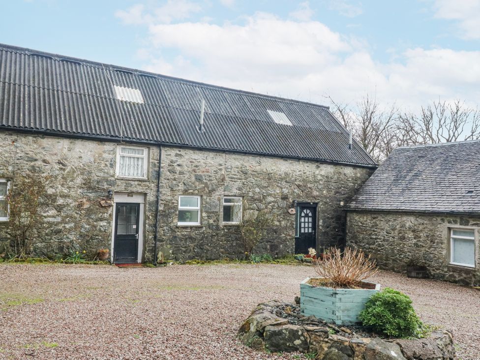 A stone building with a door and windows in a gravel courtyard at Sycamore near Killean Farmhouse Cottages in Inveraray