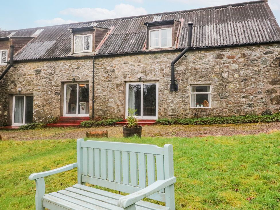 An outdoor view of a stone building with a bench and grass at Sycamore Killean Farmhouse Cottages near Inveraray