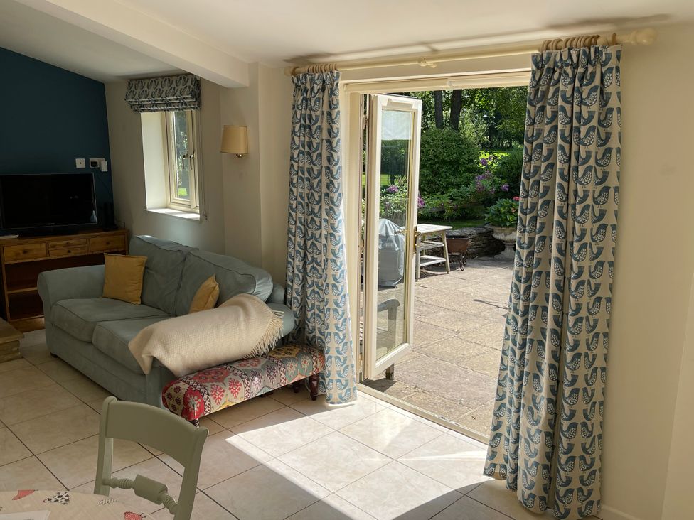 A living room with a sofa and an open door leading to the garden at Meadow Lodge, Cerney Wick near South Cerney, Cotswolds