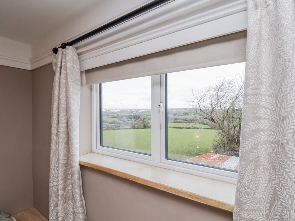 A window with curtains showing a landscape view at Ingleside Cottage in Whitby