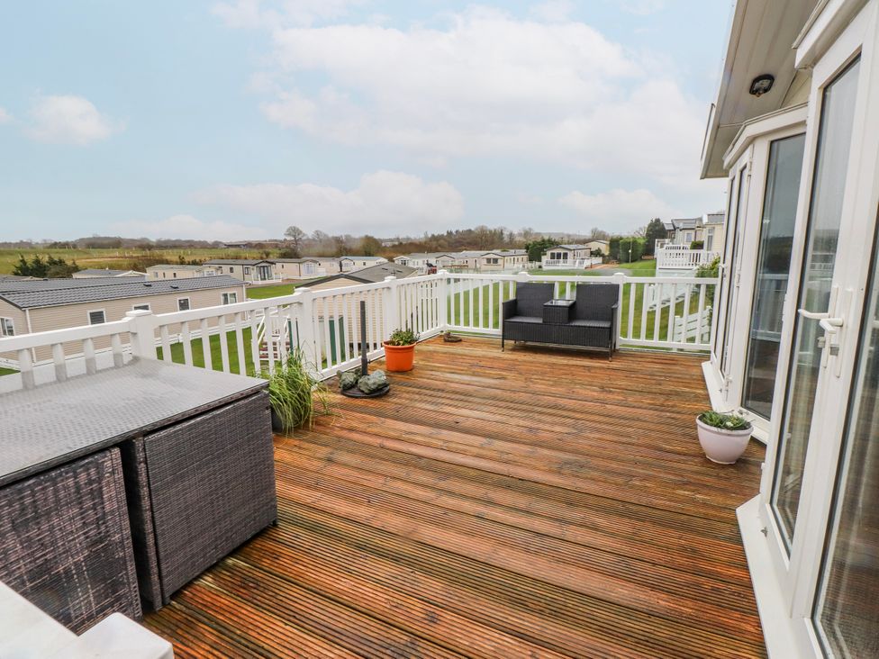 A deck with a chair and table overlooking other properties at Lodge 134 Lon Bryn Mair near Bellech
